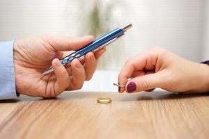 Husband is giving pen to sign divorce papers his former wife after he take off the ring form finger