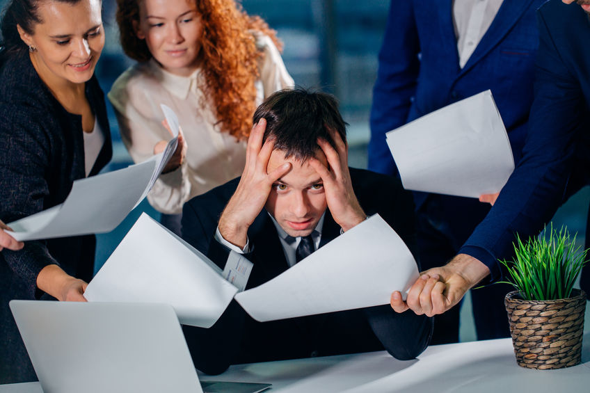 Businessman holding head with hands surrounded by worried colleagues with business documents in hands. missing deadline
