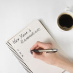 Phrase New Year's resolutions in the notebook. Female hand with pen and cup of coffee