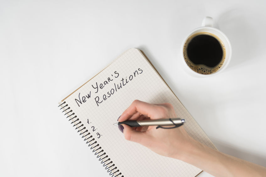 Phrase New Year's resolutions in the notebook. Female hand with pen and cup of coffee