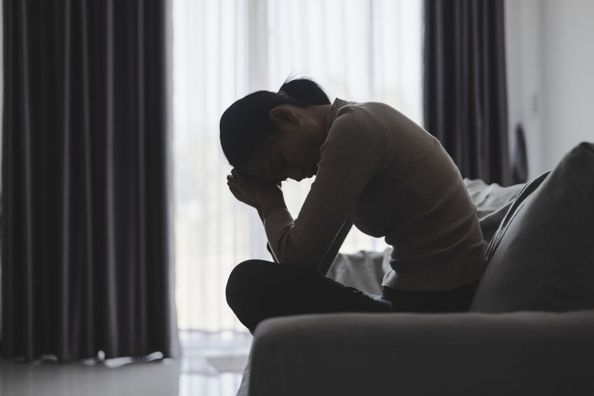 Asian young woman sitting on the sofa feeling grief.